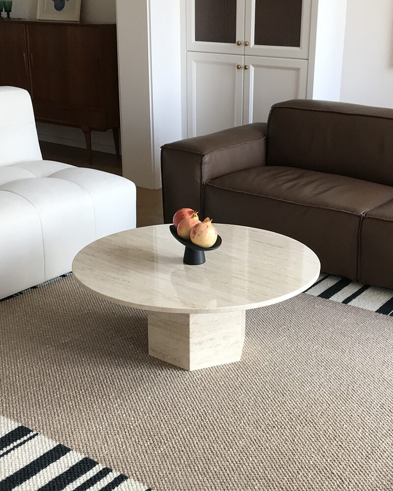 White travertine round coffee table with a hexagonal pedestal between white and brown seating