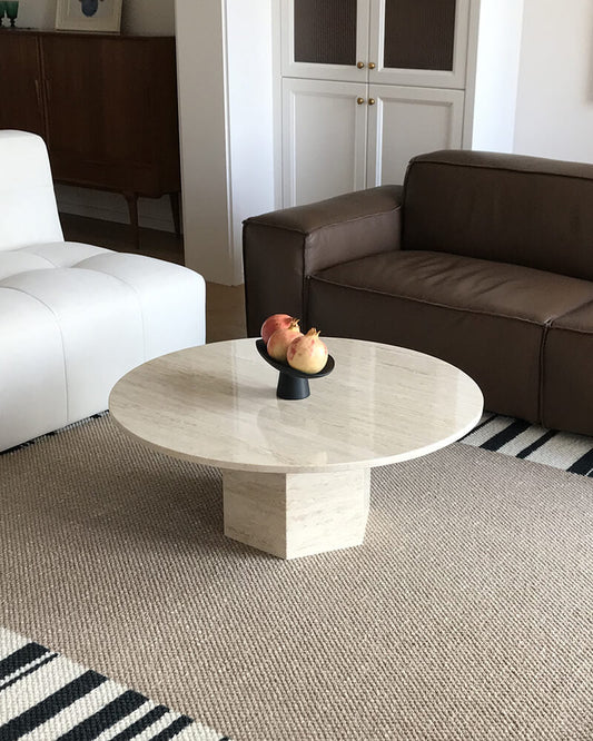 White travertine round coffee table with a hexagonal pedestal between white and brown seating