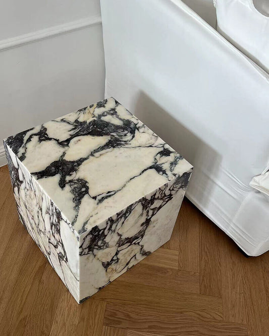 Low square marble plinth side table positioned beside a white upholstered bed