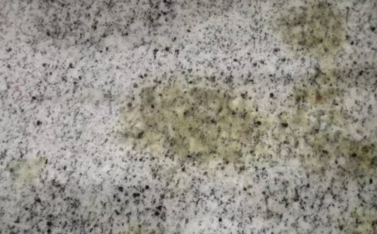 Yellow oil discoloration on a speckled natural stone surface