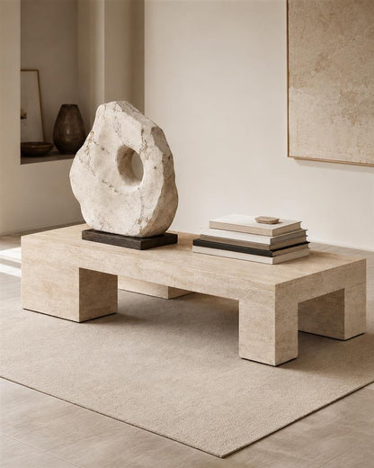 Beige travertine coffee table styled with books and a stone sculpture