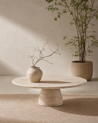 Round natural stone coffee table styled with a ceramic vase and branches