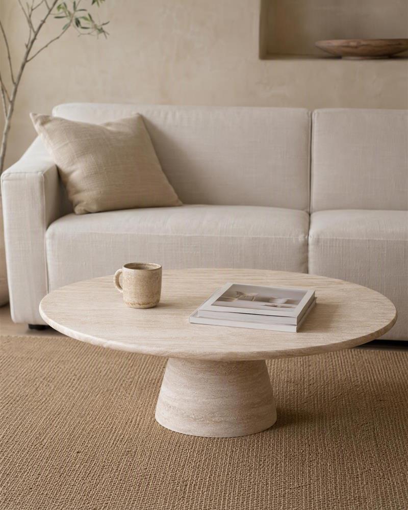 Round travertine coffee table styled with a mug and books in a neutral living room