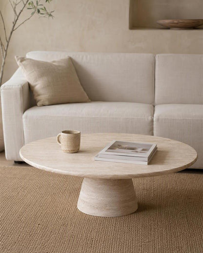 Round travertine coffee table styled with a mug and books in a neutral living room